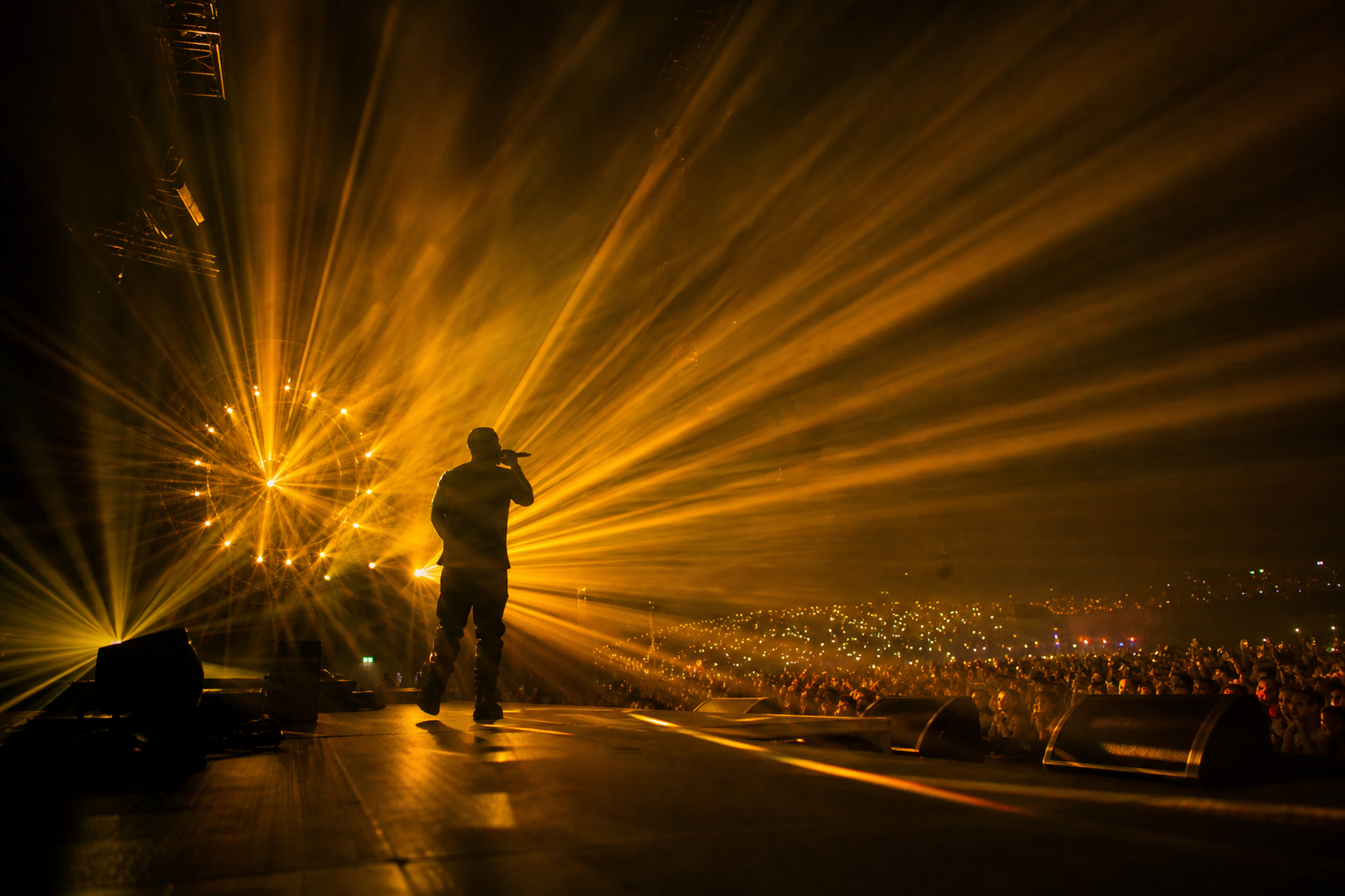 Concert venue with thick haze hanging in the air, sharp laser beams cutting through the room above a performer on stage