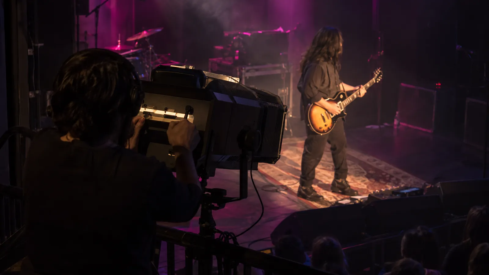 An operator aims a manual followspot at a guitarist during a concert front-light focus.